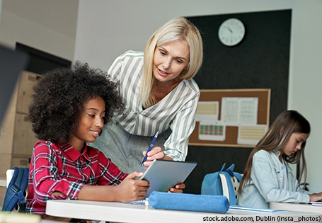Happy Afro American schoolkid listening to teacher holding tablet in classroom. HSP smart, Hamburger Schreib-Probe (HSP)